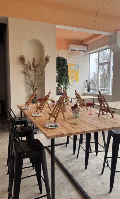 Cozy creative studio of Pigmentori — big painting table, easels, black stools, and soft natural light in a beige-peach interior