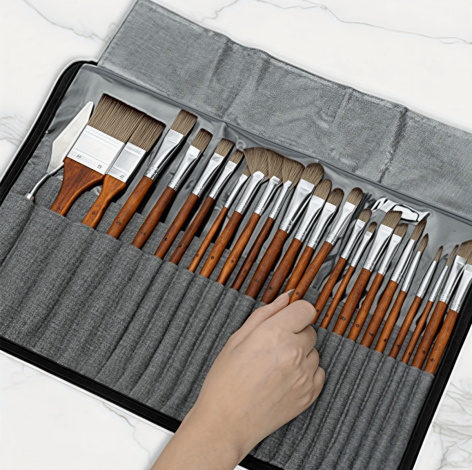 Set of paintbrushes in a gray case with a hand reaching in to pick one up.